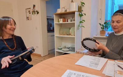 eine Ordensschwester und eine Trainerin sitzen am runden Tisch Capoerira spielend mit Trommeln