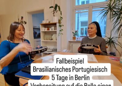 Eine Ordensschwester sitzt mit junger Frau ein brasilianisches Instrument spielend und Lernmaterialien auf dem Tisch liegend