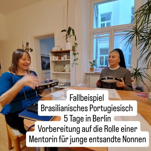 Eine Ordensschwester sitzt mit junger Frau ein brasilianisches Instrument spielend und Lernmaterialien auf dem Tisch liegend