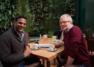 Englisch Trainer der SprachenGalerie sitzt mit Kunde im Cafe mit botanischem Garten im Hintergrund