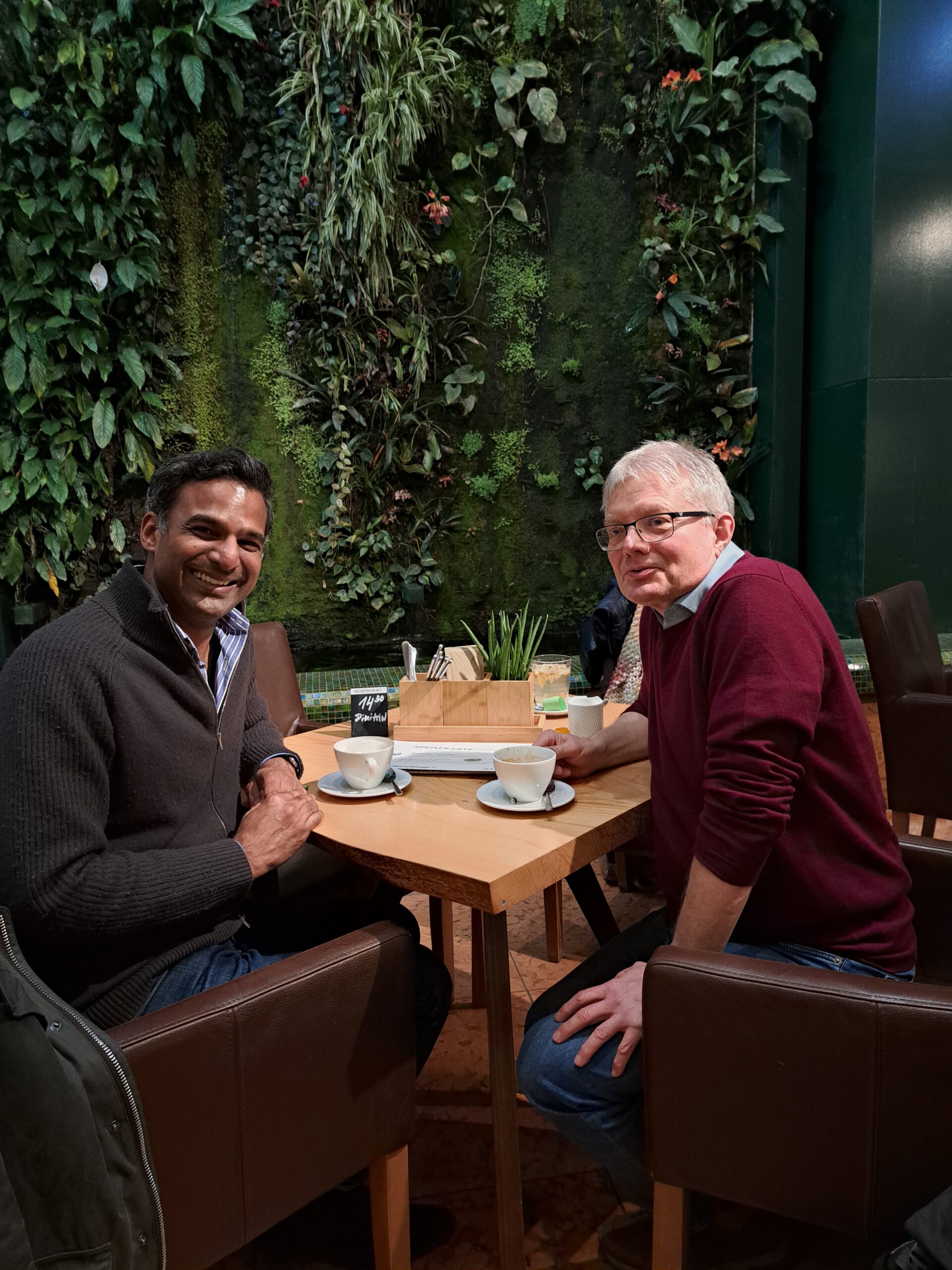 Englisch Trainer der SprachenGalerie sitzt mit Kunde im Cafe mit botanischem Garten im Hintergrund